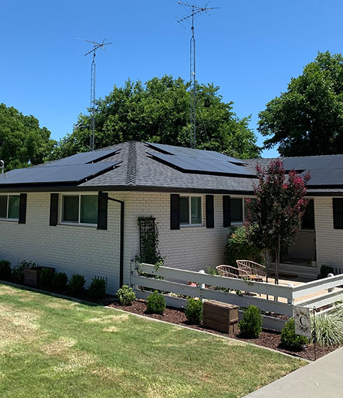 white brick house with black roofing and solar panels